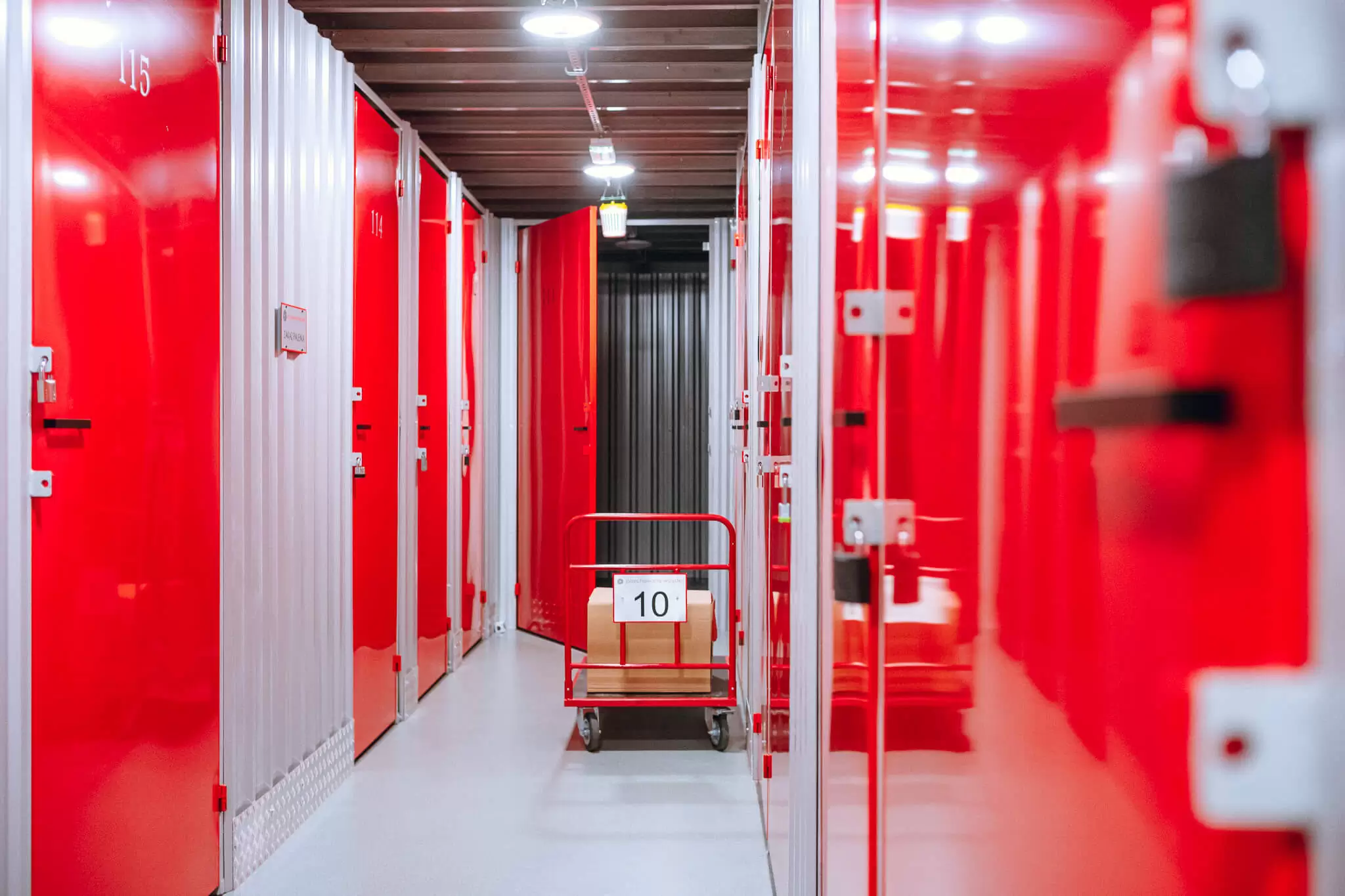 Korytarz z czerwonymi drzwiami boksów i wózkiem transportowym w Celtic Self Storage Piaseczno